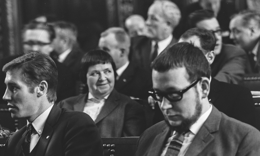 Inmitten männlicher Parlamentsmitglieder sitzt Gertrud Spiess auf ihrem Sitz im Grossratssaal.