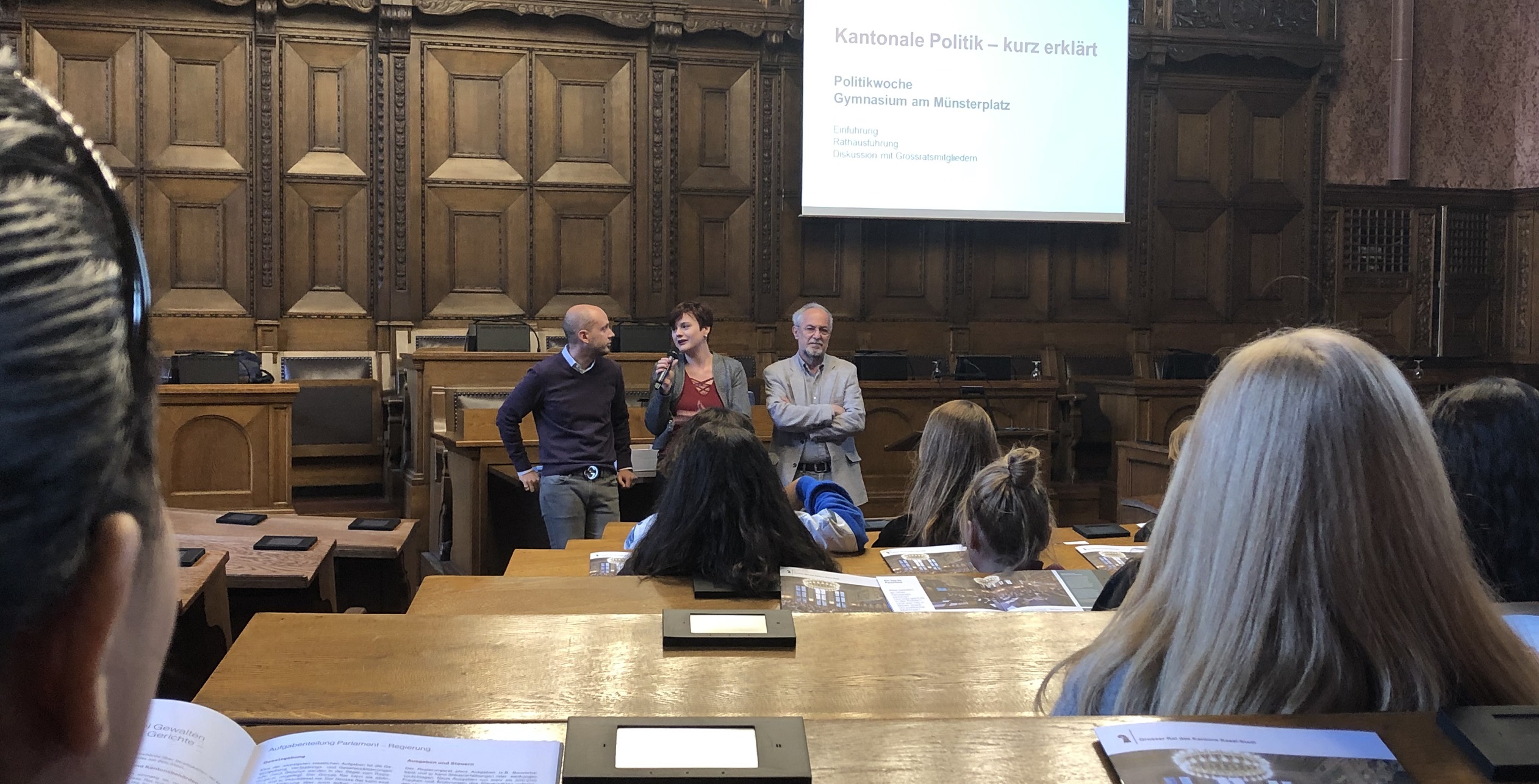 Drei Grossratsmitglieder debattieren im Grossratssaal mit Schulklassen.