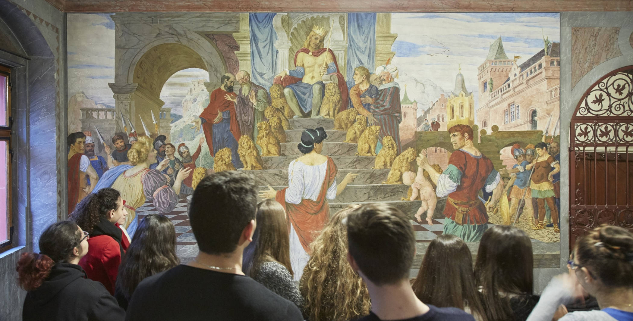 Schülerinnen und Schüler betrachten bei einem Besuch im Rathaus das Wandbild "König Salomon".